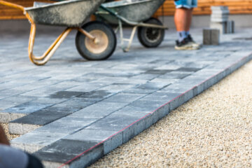 Laying gray concrete paving slabs in house courtyard driveway patio.