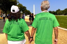 From left to right a woman and man wearing green shirts stand facing a distant Washington Monument on a clear day