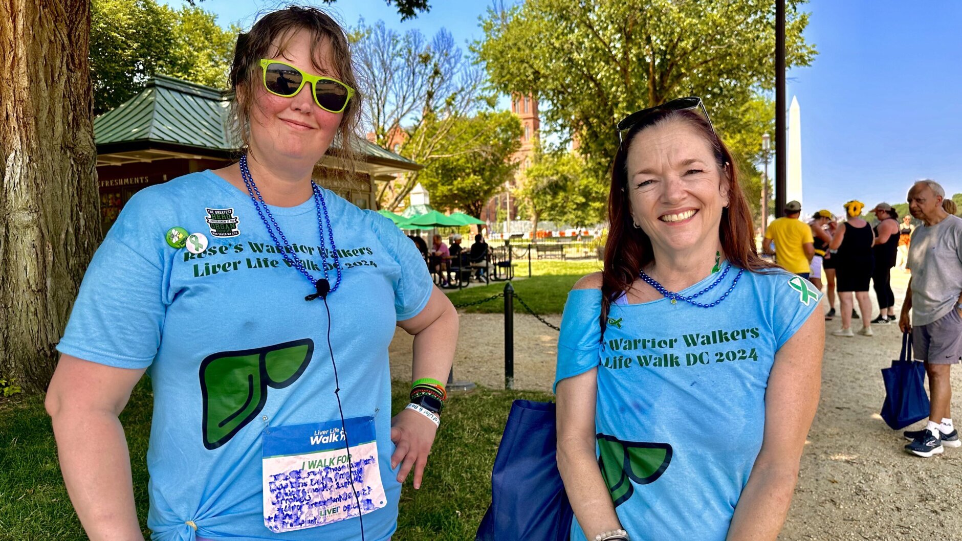 Dois sobreviventes de transplante vestindo camisetas azuis ficam em frente a um parque