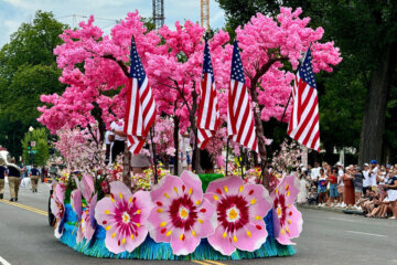 a parade float with large cherry blossom flower cutouts and faux trees along with American flags