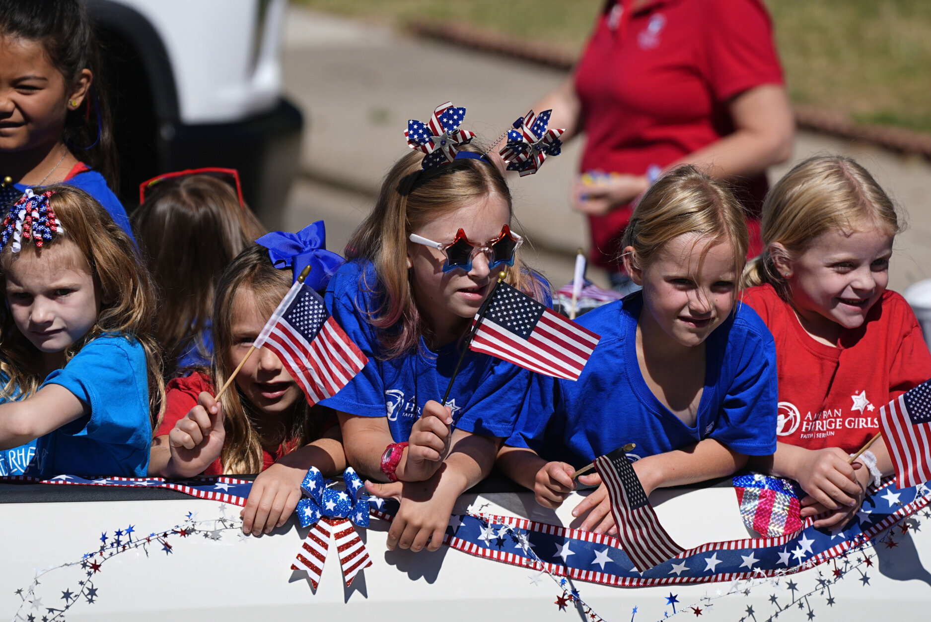 kids huddled together are dressed in red, white and blue, carrying American flags