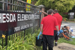 People cleaning anti-Israel and antisemitic graffiti from an elementary school sign.