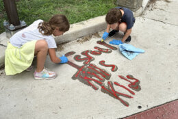 Two children cleaning graffiti from sidewalk