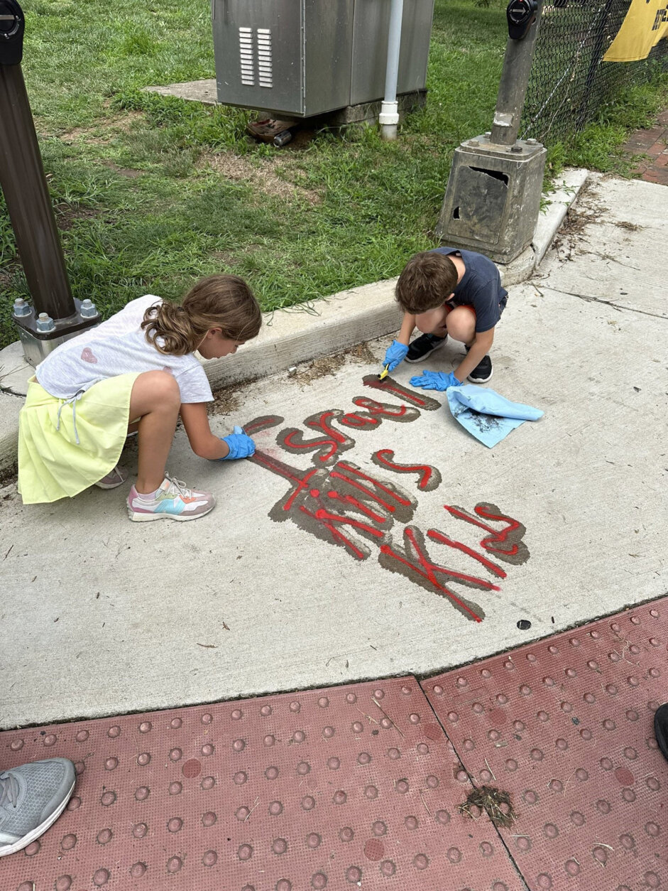 Two children cleaning graffiti from sidewalk