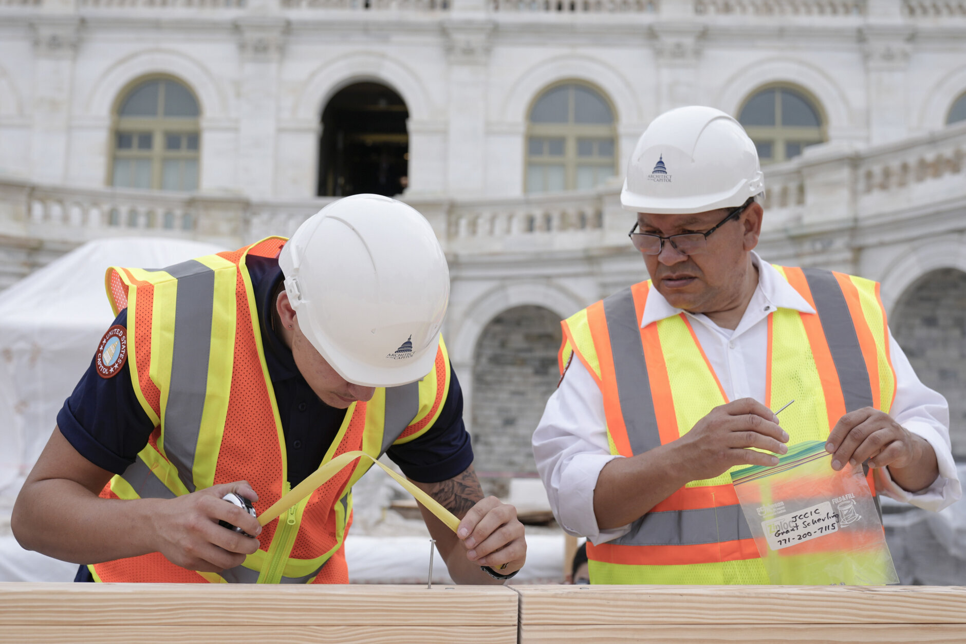 Tyler Smith, a woodcrafter with the Architect of the Capitol, and Herbert Melgar, a painter, measure out the nail placement for Congress members to hammer for the First Nail Ceremony marking the beginning of construction of the 2025 Presidential Inauguration platform at the Capitol, Wednesday, Sept. 18, 2024, in Washington. (AP Photo/Mariam Zuhaib)