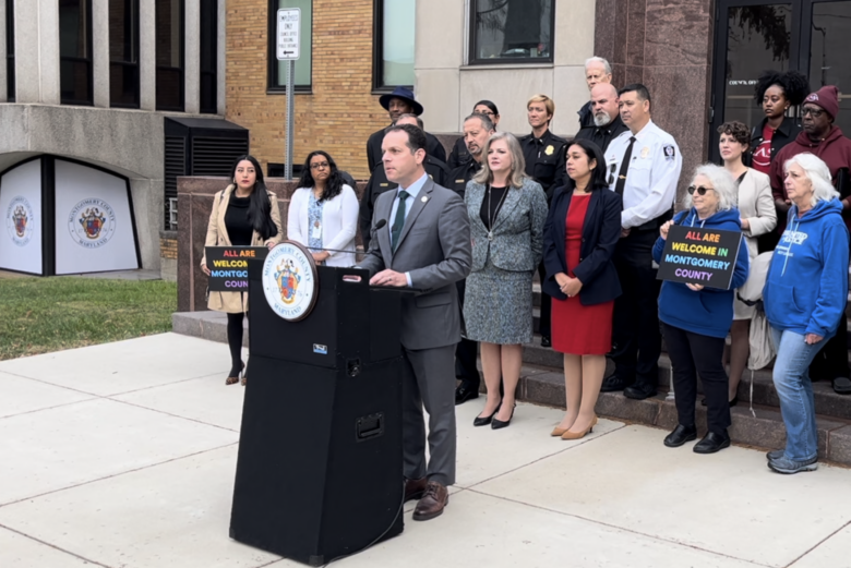 Evan Glass speaks at podium with supporters behind