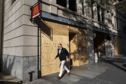 A pedestrian walks past stores open for business but boarded up with wood, near the White House in Washington, Monday, Nov. 4, 2024, in advance of Election Day. (AP Photo/Ben Curtis)