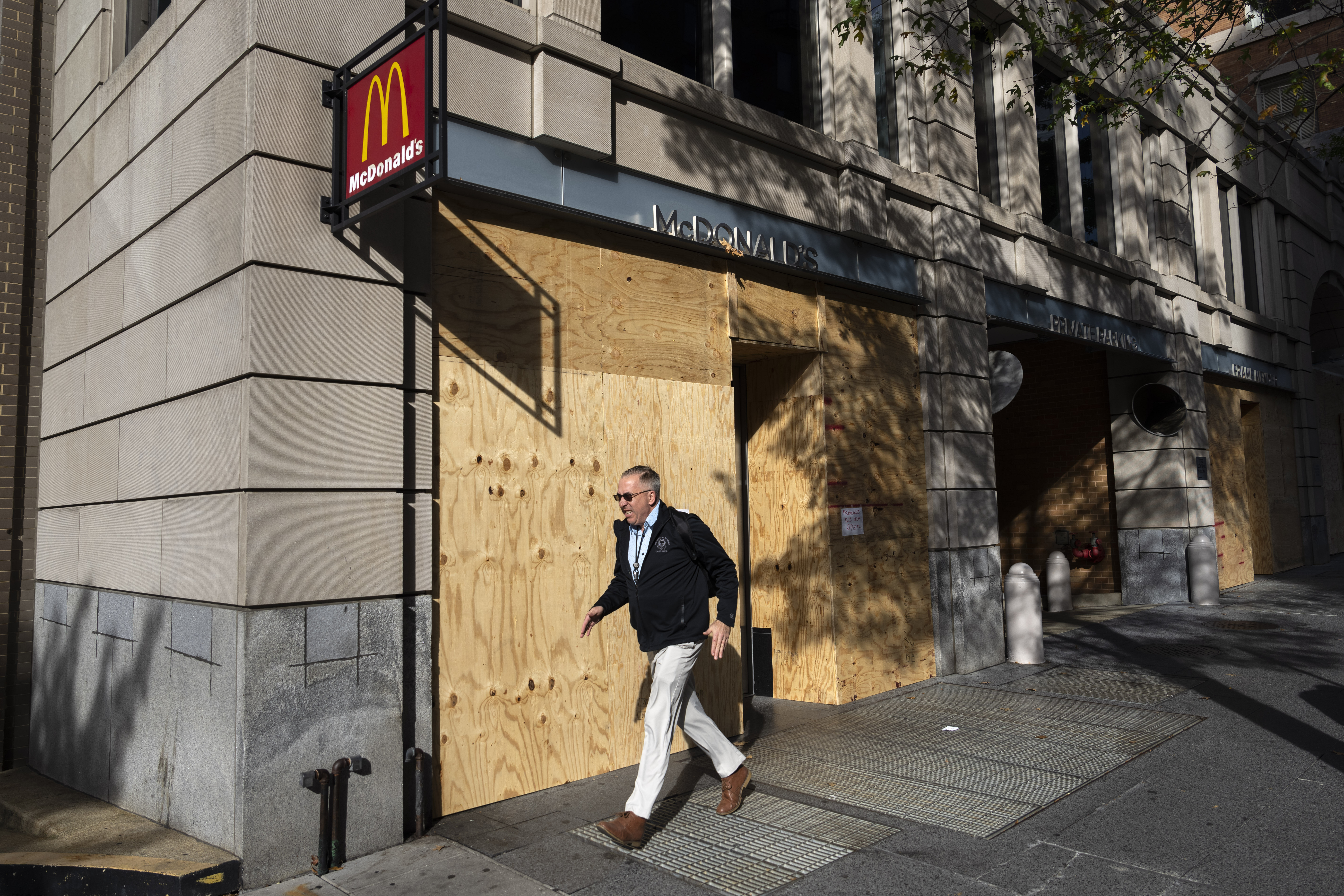 A pedestrian walks past stores open for business but boarded up with wood, near the White House in Washington, Monday, Nov. 4, 2024, in advance of Election Day. (AP Photo/Ben Curtis)