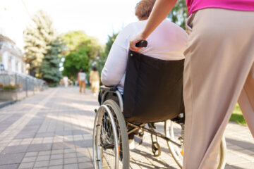 Young female caregiver pushing wheelchair with women with disability.