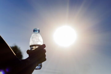 Bottle with water in a woman's hand against the bright sun