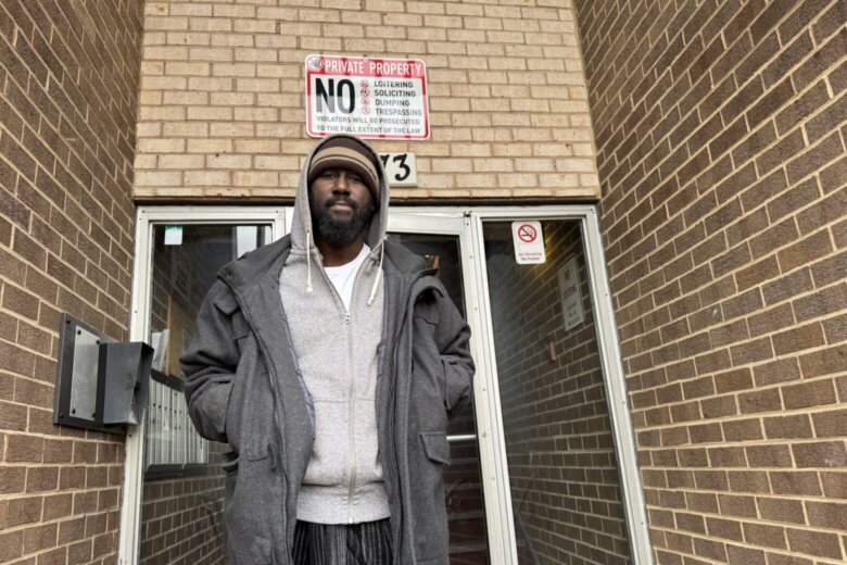 man stands heavily bundled in winter clothing outside apartment building