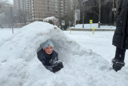 child sits in fort built out of snow