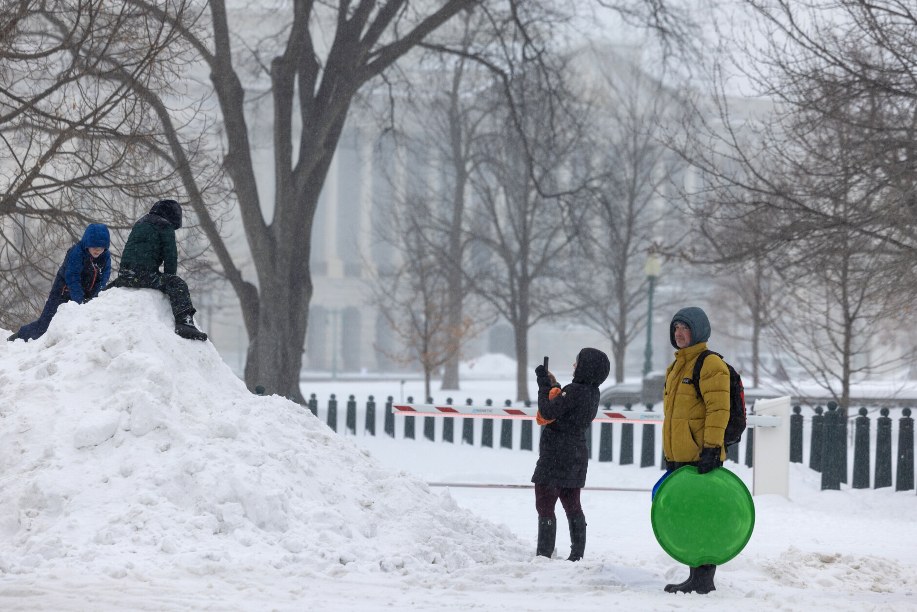 children play on big pile of snow as parents watch from side