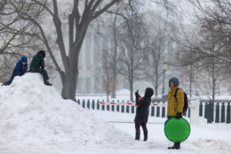 children play on big pile of snow as parents watch from side