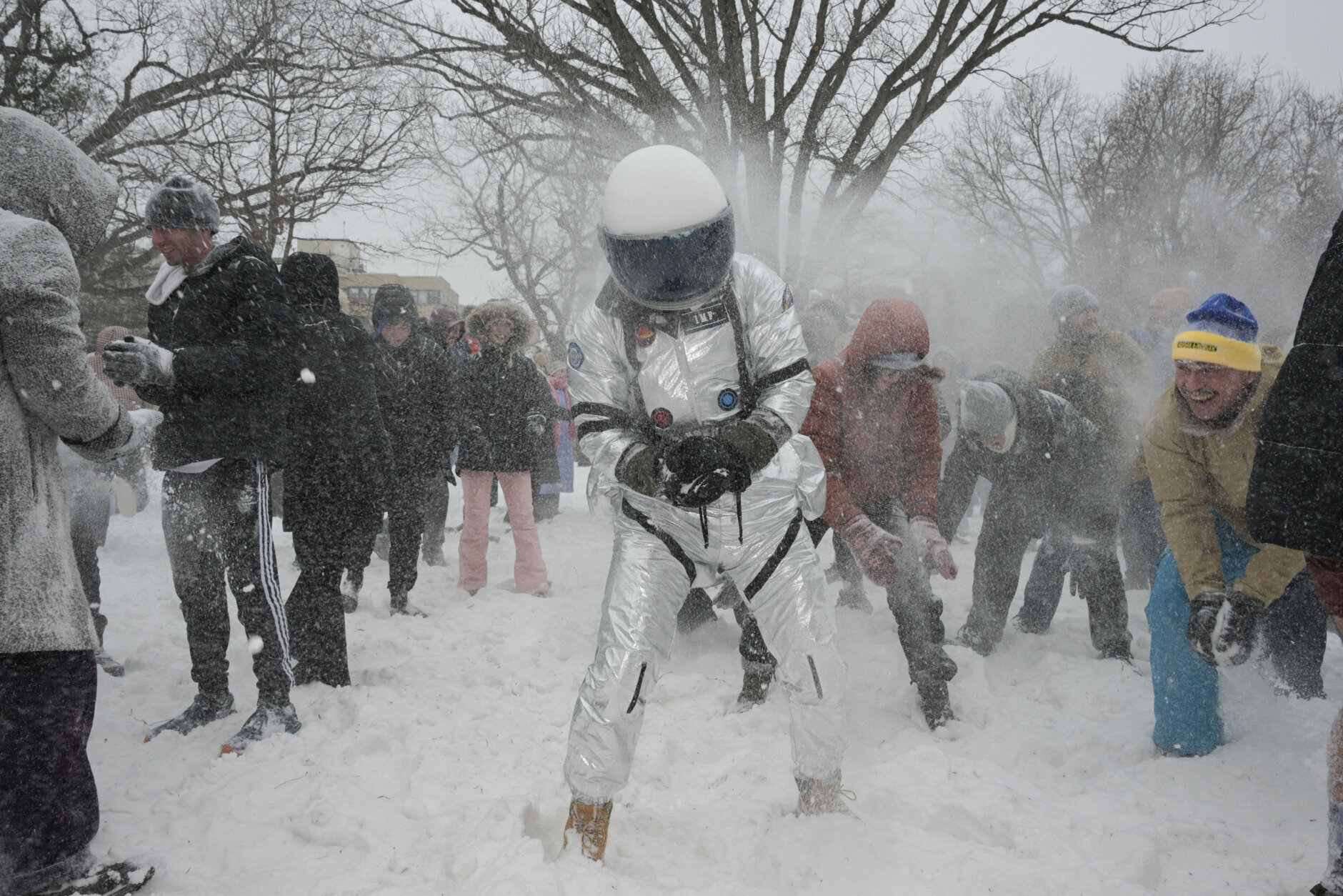 person wearing astronaut gear gets hit with snow balls during big snow ball fight