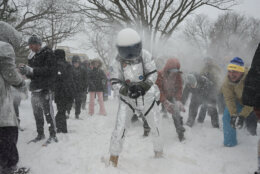 person wearing astronaut gear gets hit with snow balls during big snow ball fight