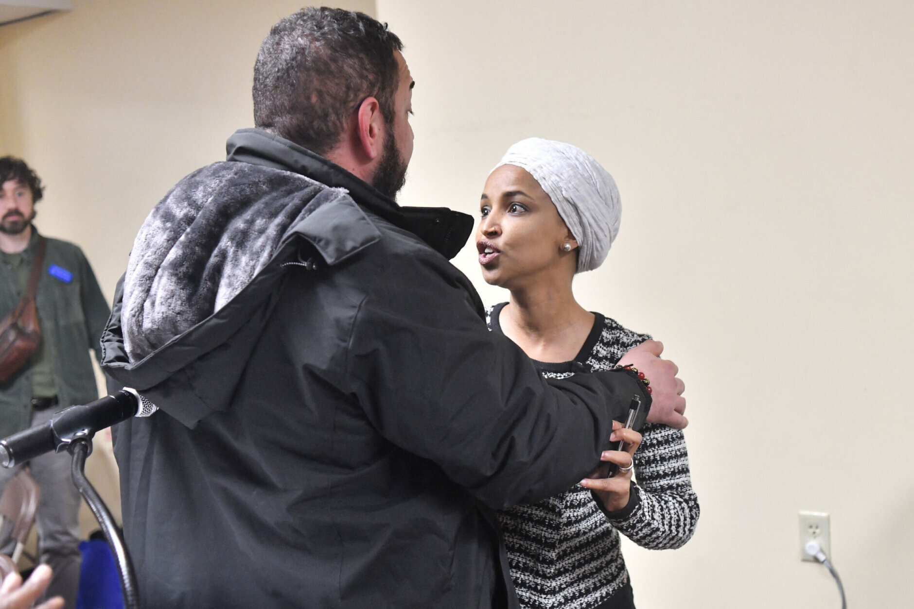 US Representative Ilhan Omar (D-MN) (R) reacts after being sprayed with an unknown substance by a man as she hosted a town hall in Minneapolis, Minnesota, on January 27, 2026. US Democratic congresswoman Ilhan Omar was targeted during a speech late on January 27 by a man who sprayed an unidentified liquid at her from a syringe before being tackled by security guards, according to an AFP journalist at the scene. The man was led out of the premises as Omar, a frequent target of attacks by President Donald Trump, continued her speech saying "we will stay resilient in the face of whatever they might throw on us." (Photo by Octavio JONES / AFP via Getty Images)