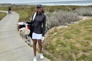 young woman golfer carrying golf bag on course with beach in background