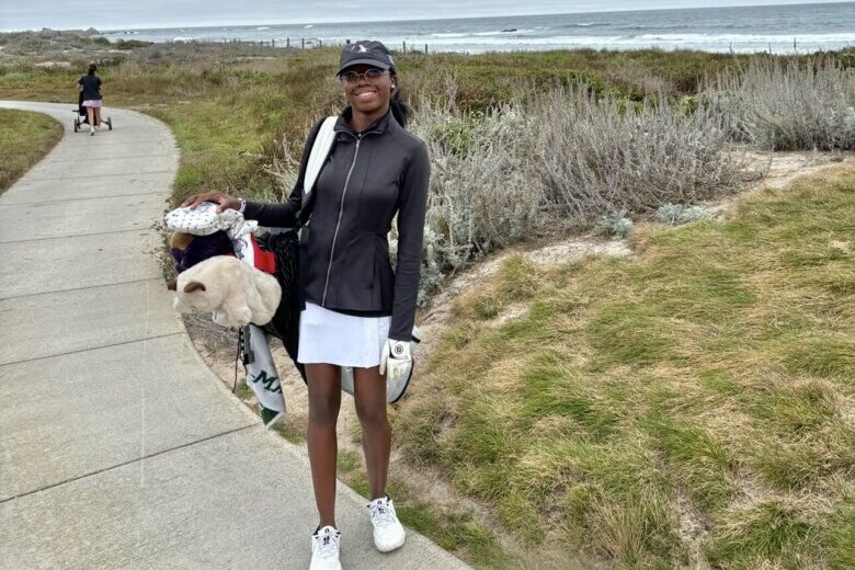 young woman golfer carrying golf bag on course with beach in background