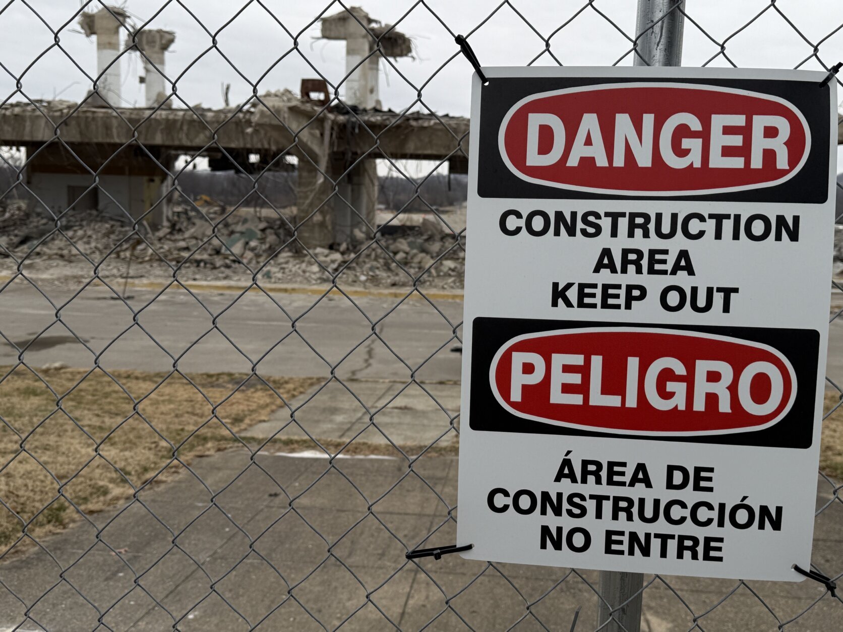 warning sign of construction area on fence with demolished structure in background