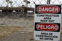 warning sign of construction area on fence with demolished structure in background