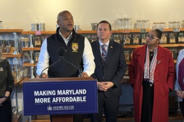 man stands behind podium with other leaders around in grocery store