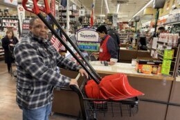 man with two shovels in shopping cart checks out at store