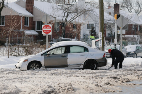 person shoveling snow around car stuck in snow