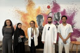 people stand for picture in front of wall with mural art of tennis player