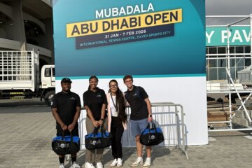 three young people standing holding duffel bags posing for picture below sign