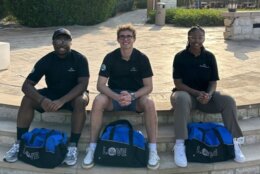 three young people sitting on a curb with duffel bags between legs.