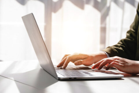 hands typing on keyboard of laptop in room with lots of natural light
