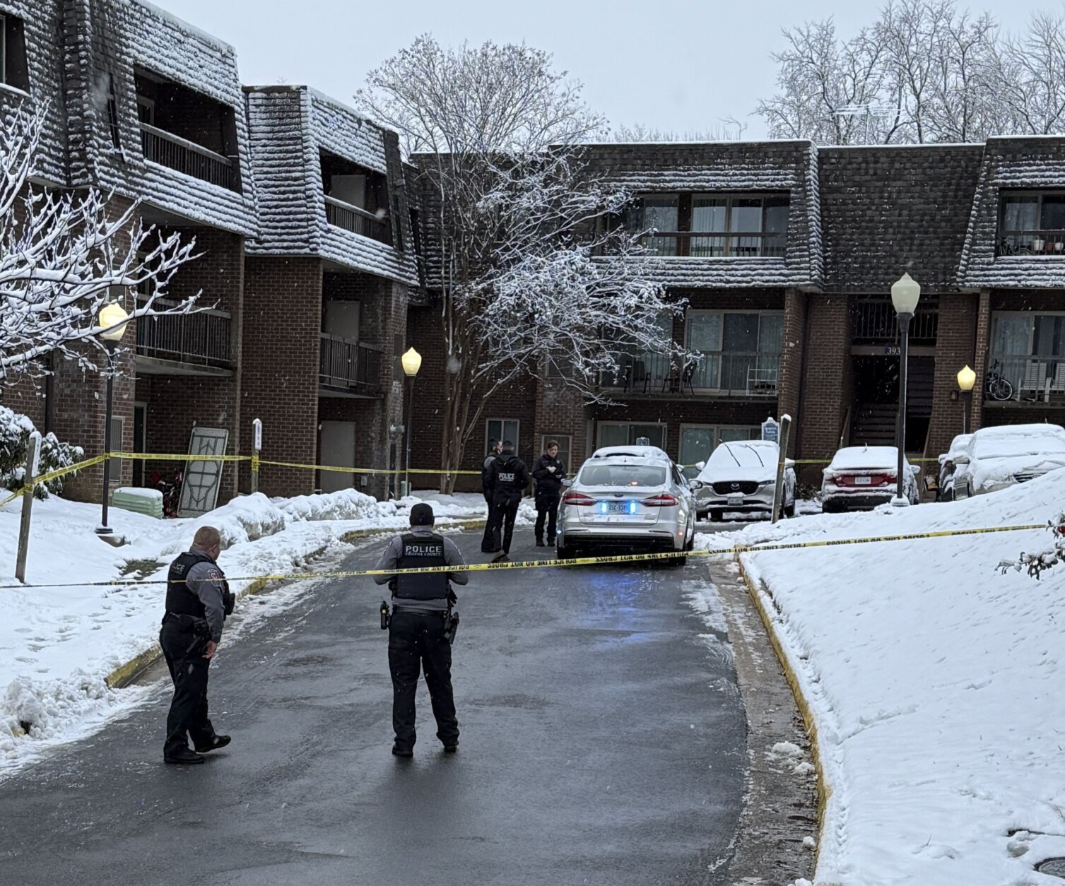 officers standing outside of apartment with crime tape and police crusiers