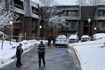 officers standing outside of apartment with crime tape and police crusiers