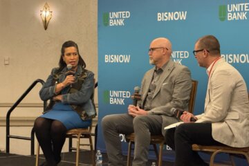 three people sit on chairs on stage holding microphones for publicized discussion