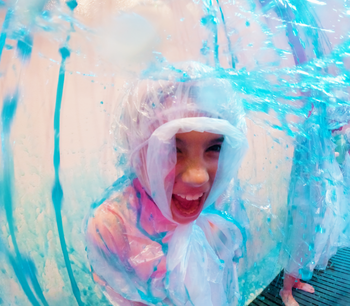 child in plastic poncho gets sprayed with bright blue slime