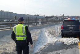 police officer looks at mound of snow on highway shoulder with tire tracks from crash