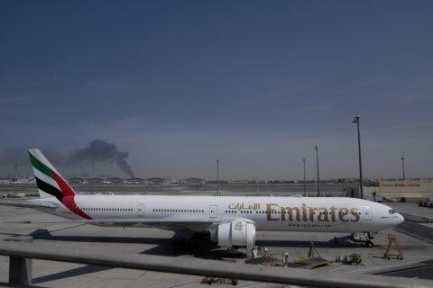 A plume of smoke caused by an Iranian strike is seen in the background an an Emirates plane is parked at the Dubai International Airport