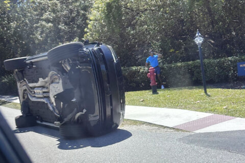 Golfer Tiger Woods stands by his overturned vehicle in Jupiter Island, Fla., on Friday, March 27, 2026. (AP Photo/Jason Oteri)