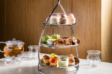 an afternoon tea service, beautifully arranged on a modern, three-tiered silver stand shaped like a drop