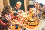Front view of friends group tasting christmas sweets food and having fun at home drinking champagne sparkling wine - Winter holidays concept with people enjoying time eating together - Warm filter