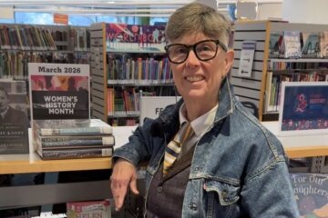 woman stands by shelf in library with books on top