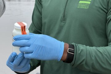 shot of person face not shown wearing surgical gloves holding sample of water in white container