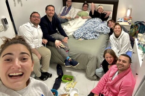 woman takes selfie with room full of friends in a bedroom