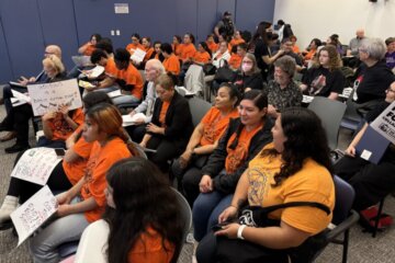 people in orange shirts with signs sit in a room