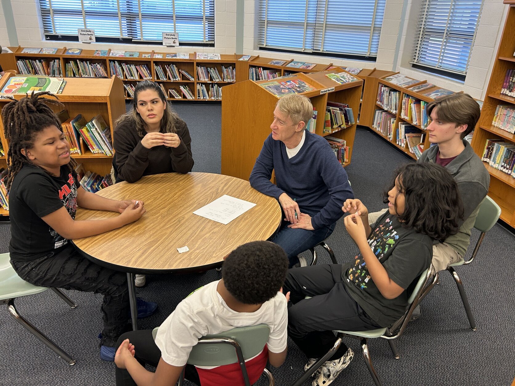 Man sitting with students at a table in school library.