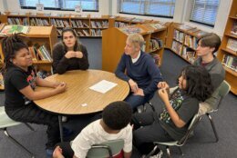 Man sitting with students at a table in school library.