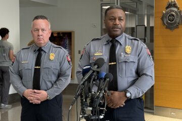two police officers speak behind microphones