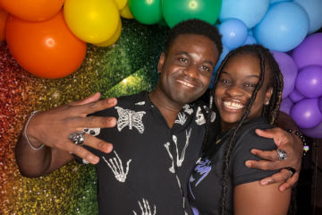 a man and a woman pose in front of a rainbow wall
