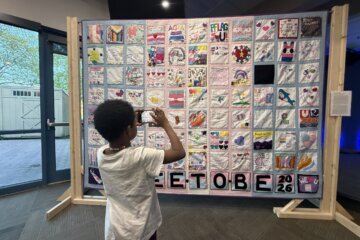 a child takes a photo of a hanging quilt